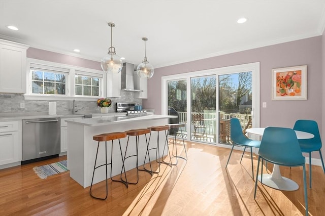 kitchen with wall chimney exhaust hood, appliances with stainless steel finishes, white cabinetry, and crown molding