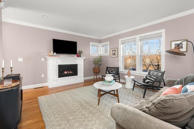 living room with a warm lit fireplace, light wood-style flooring, and ornamental molding