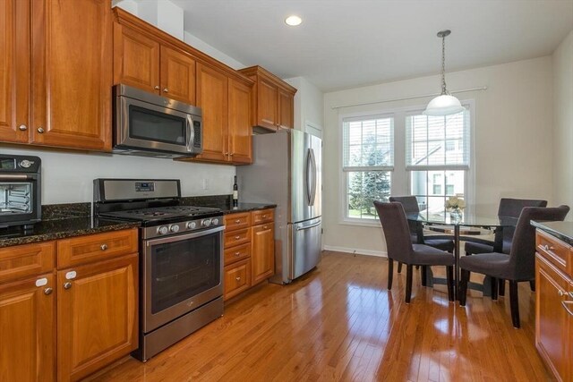 25 Kelly Way Unit 25, Canton, MA 02021 - kitchen featuring appliances with stainless steel finishes, brown cabinetry, light wood-type flooring, decorative light fixtures, and dark stone counters