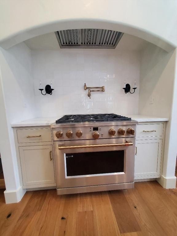 kitchen with decorative backsplash, high end stainless steel range, and light hardwood / wood-style flooring