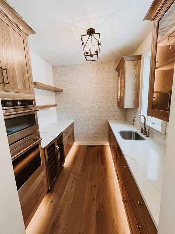 kitchen featuring an inviting chandelier, sink, decorative light fixtures, light stone counters, and stainless steel double oven