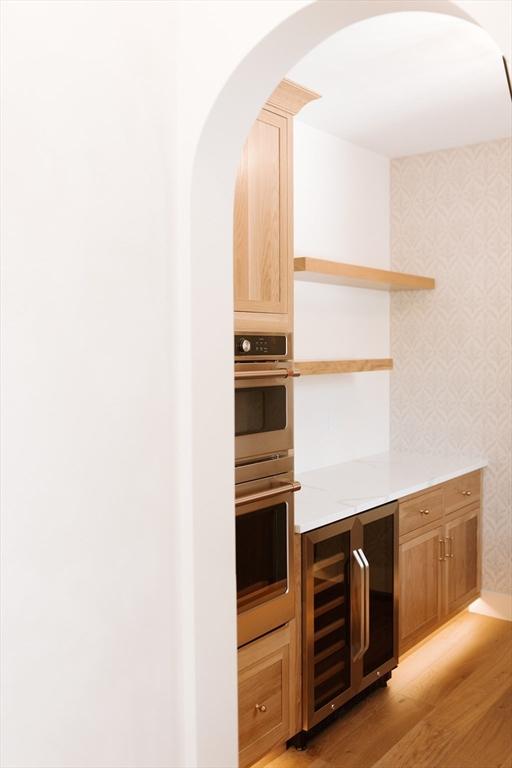 kitchen featuring stainless steel double oven, light wood-type flooring, and beverage cooler