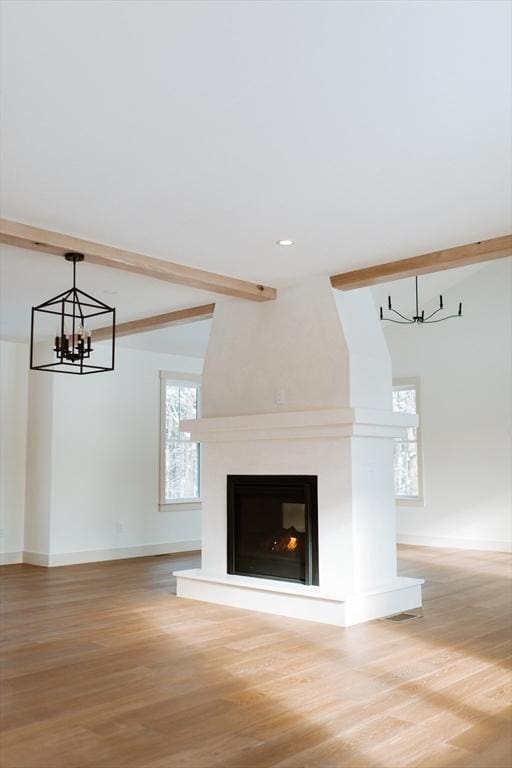 unfurnished living room featuring hardwood / wood-style flooring, lofted ceiling with beams, a large fireplace, and a chandelier