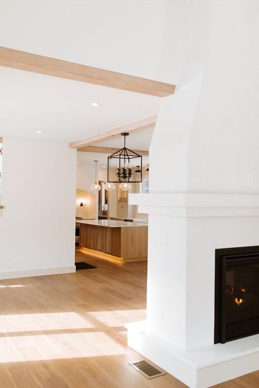 interior space with light wood-type flooring, beam ceiling, light brown cabinets, an inviting chandelier, and hanging light fixtures