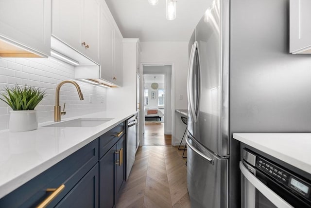 kitchen featuring stainless steel appliances, light countertops, decorative backsplash, white cabinets, and a sink