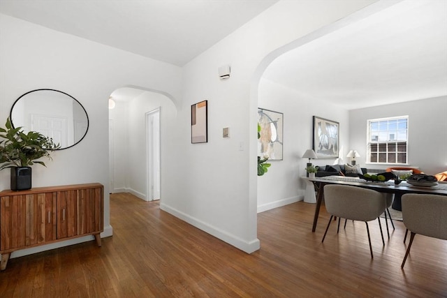 corridor featuring arched walkways, wood finished floors, and baseboards