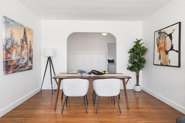 dining area with arched walkways, wood finished floors, and baseboards