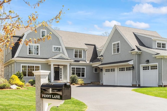 shingle-style home featuring driveway, roof with shingles, a gambrel roof, a front lawn, and an attached garage