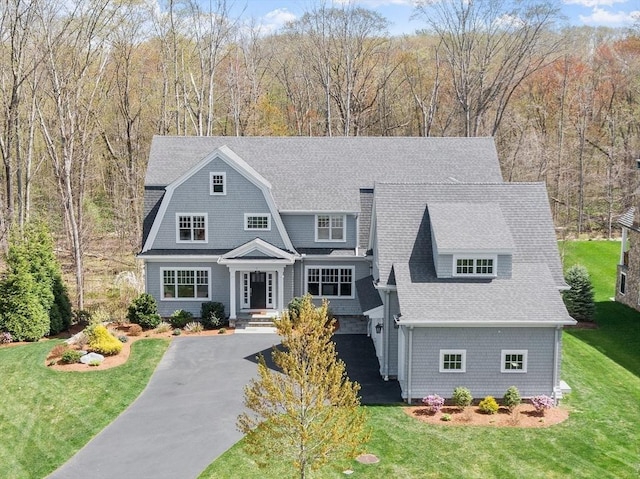 view of front of home with aphalt driveway, a front lawn, and roof with shingles