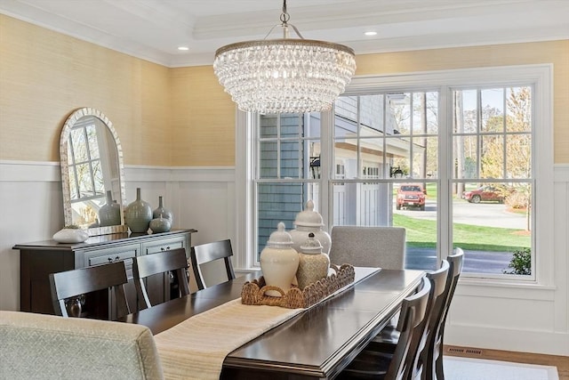 dining area with a healthy amount of sunlight, ornamental molding, a decorative wall, and a chandelier