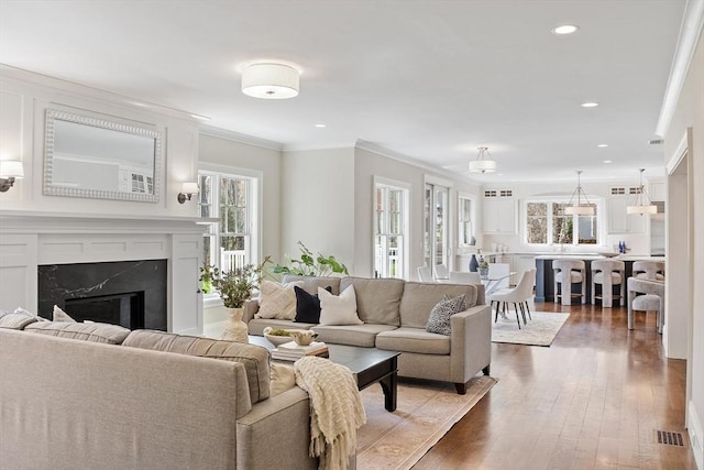living area featuring visible vents, a fireplace, ornamental molding, recessed lighting, and hardwood / wood-style floors