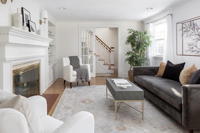 living room featuring wood finished floors, stairs, built in shelves, ornamental molding, and baseboards