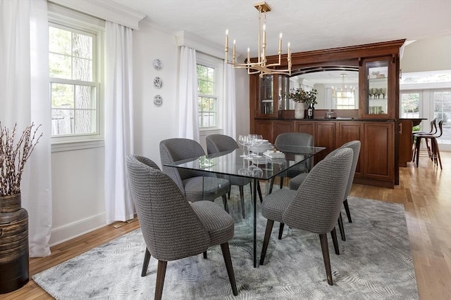 dining area featuring a chandelier, light wood-style flooring, baseboards, and ornamental molding