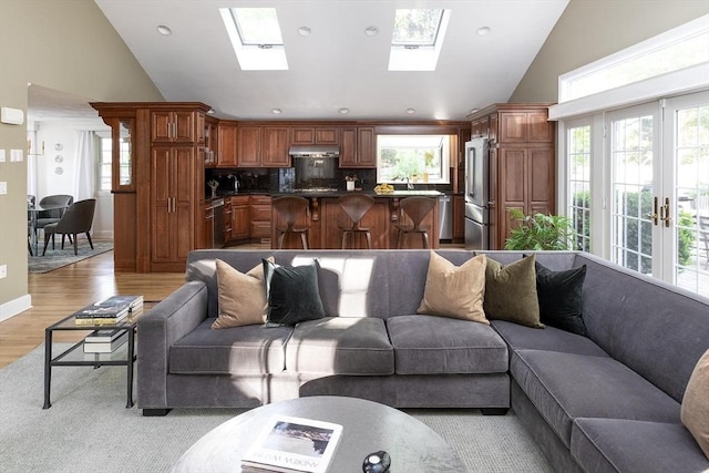 living room with vaulted ceiling, light wood finished floors, a skylight, recessed lighting, and french doors