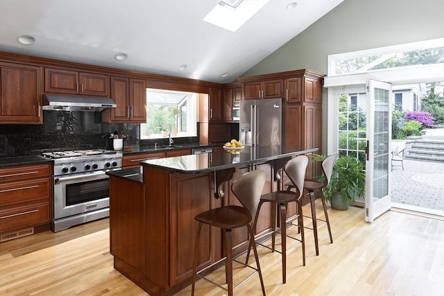 kitchen featuring stainless steel appliances, under cabinet range hood, a skylight, decorative backsplash, and a breakfast bar