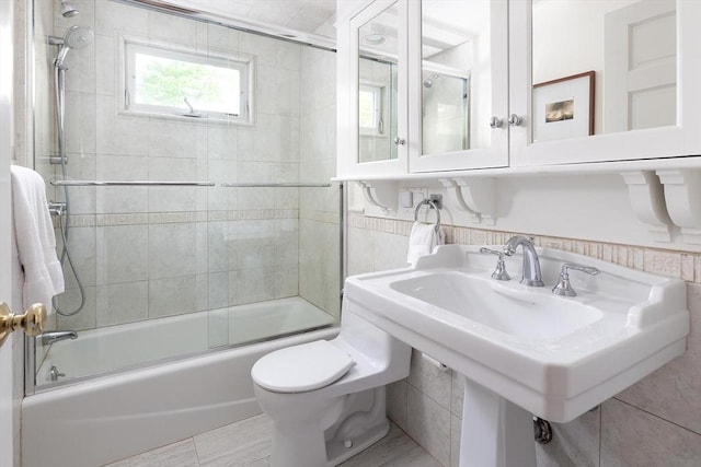 bathroom with combined bath / shower with glass door, toilet, and tile walls