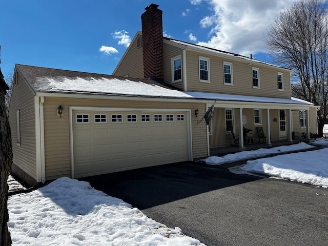 view of front of house with a garage, covered porch, a chimney, and aphalt driveway