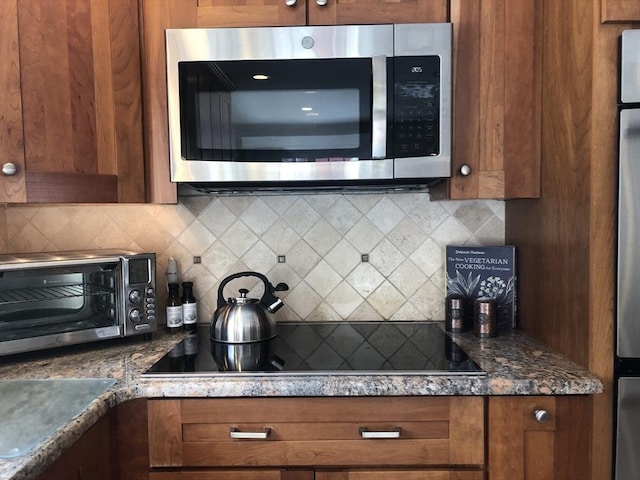 kitchen featuring tasteful backsplash, black electric stovetop, stainless steel microwave, and brown cabinets