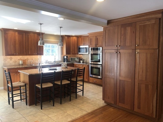 kitchen featuring stone countertops, a center island with sink, appliances with stainless steel finishes, a breakfast bar, and decorative light fixtures