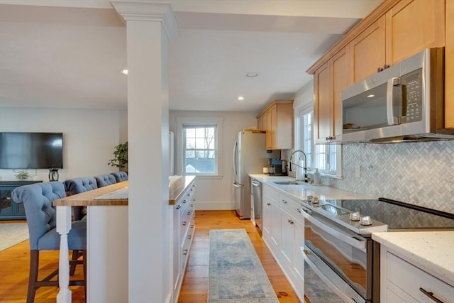 kitchen featuring sink, appliances with stainless steel finishes, backsplash, a kitchen bar, and light brown cabinets