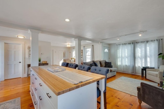 kitchen with a breakfast bar, decorative columns, butcher block counters, white cabinets, and light hardwood / wood-style flooring