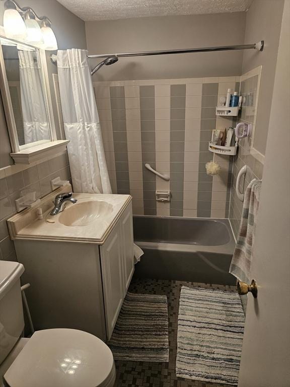 bathroom with toilet, a textured ceiling, shower / tub combo, vanity, and tile walls