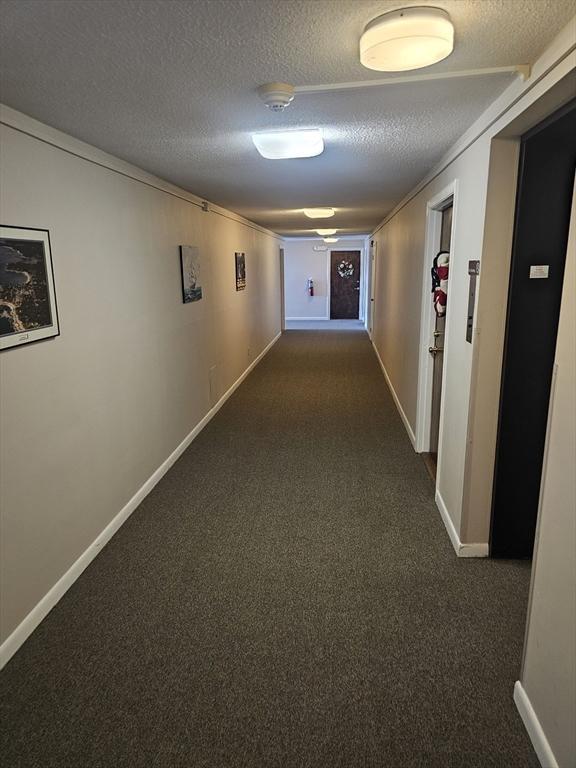 corridor with a textured ceiling, baseboards, and dark colored carpet
