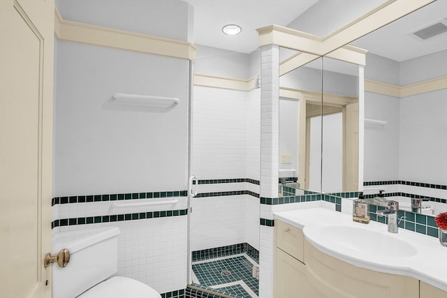 bathroom featuring tile patterned flooring, toilet, tile walls, a shower with shower door, and vanity