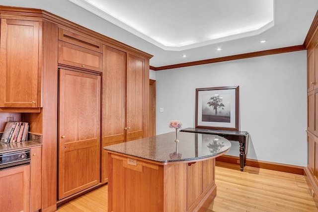 kitchen with crown molding, a kitchen island, dark stone countertops, and light wood-type flooring