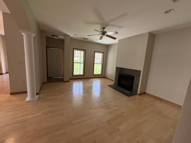 unfurnished living room with baseboards, ornate columns, light wood-type flooring, a tile fireplace, and a ceiling fan