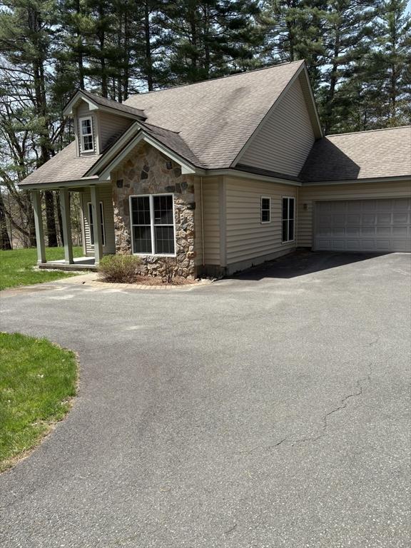 craftsman-style home with a garage, driveway, roof with shingles, and stone siding