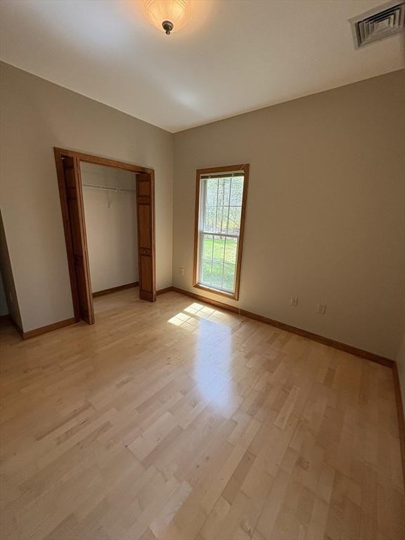 unfurnished bedroom with baseboards, a closet, light wood-style flooring, and visible vents