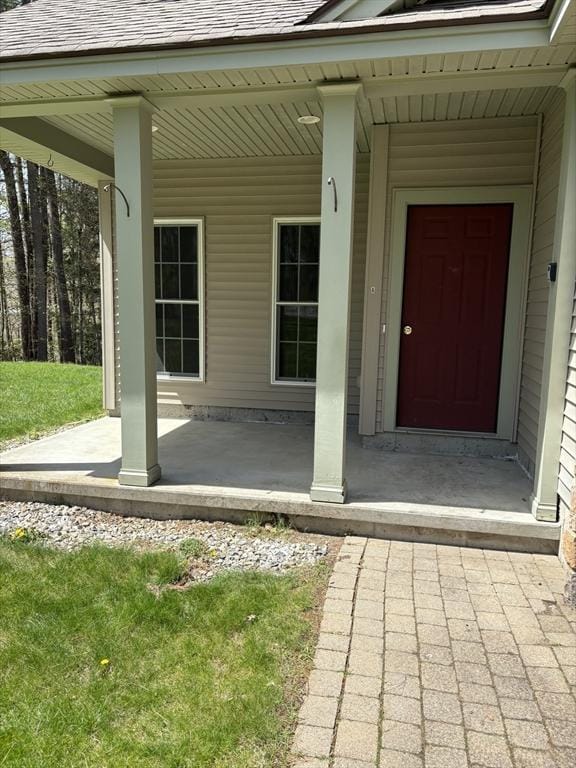 entrance to property with covered porch and a shingled roof