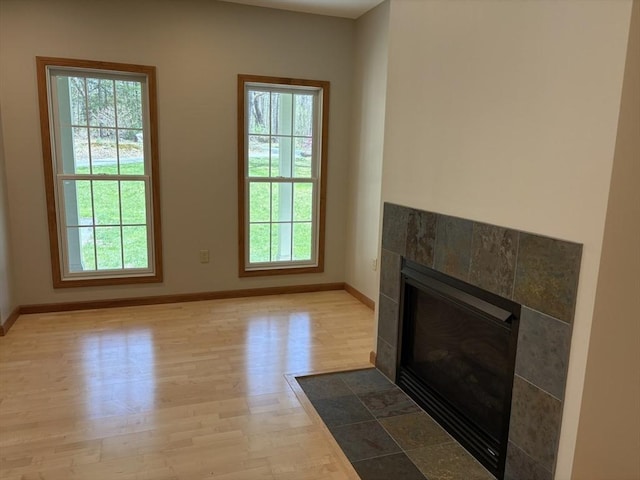 unfurnished living room with a healthy amount of sunlight, baseboards, a tile fireplace, and wood finished floors