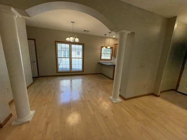 unfurnished dining area with decorative columns, visible vents, arched walkways, baseboards, and light wood finished floors