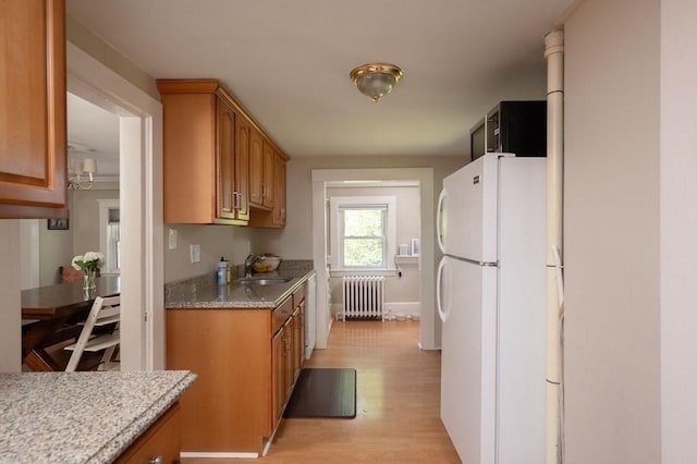 kitchen featuring white fridge, light wood-type flooring, radiator, light stone counters, and sink