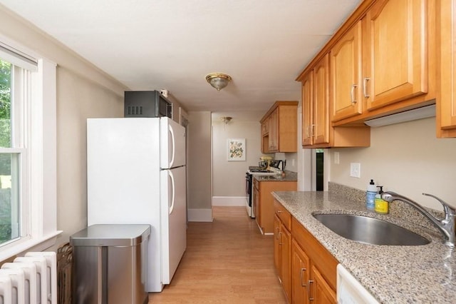 kitchen with white appliances, light hardwood / wood-style floors, radiator heating unit, light stone counters, and sink