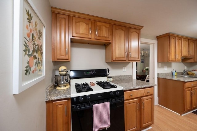 kitchen featuring gas range, light hardwood / wood-style floors, light stone counters, and sink