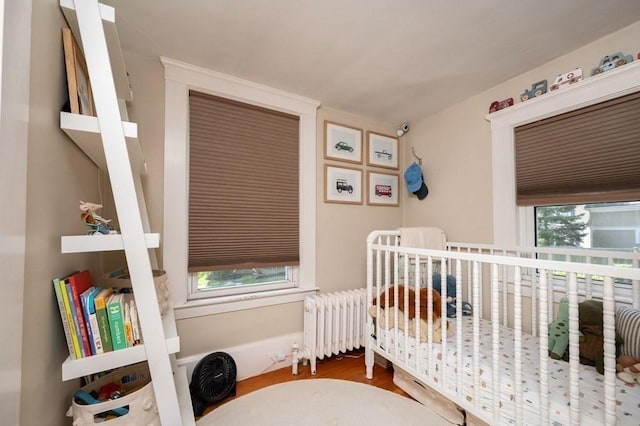 bedroom featuring radiator, a nursery area, and hardwood / wood-style floors