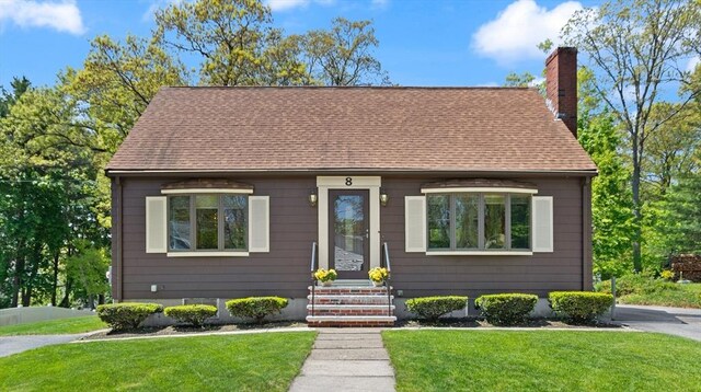 view of front of home with a chimney, a front lawn, and roof with shingles