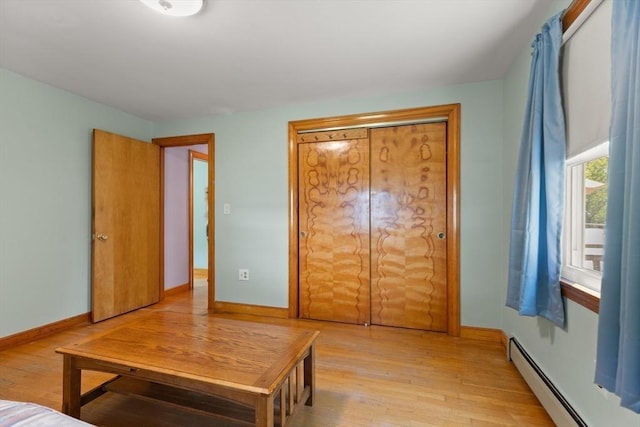 unfurnished bedroom featuring a baseboard heating unit, light wood-type flooring, and baseboards