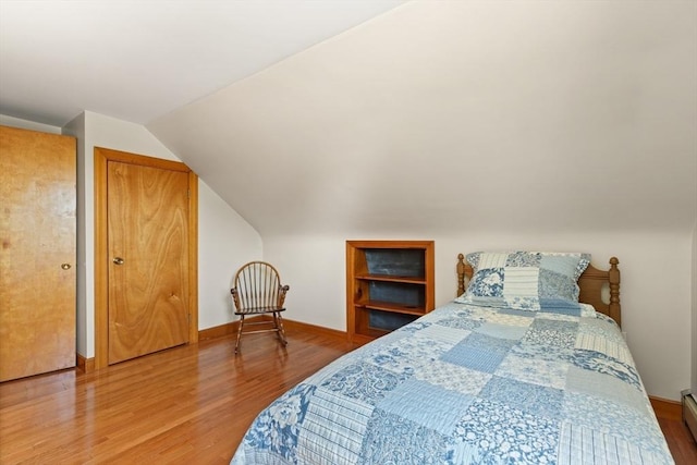 bedroom with wood finished floors, lofted ceiling, baseboards, and a baseboard heating unit