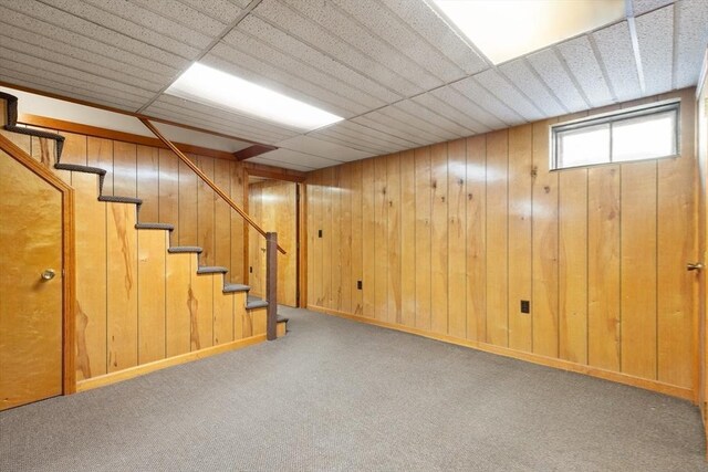 basement featuring carpet floors, stairs, and wooden walls