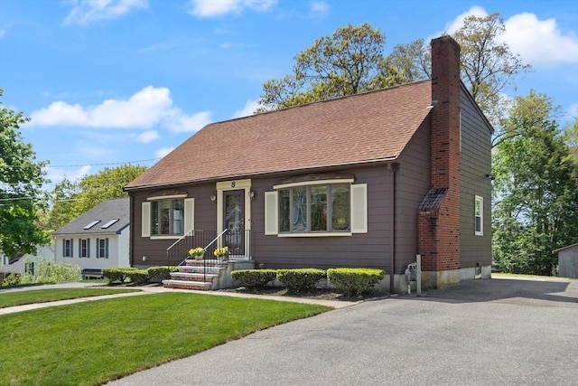 view of front of house featuring a chimney, a front yard, asphalt driveway, and a shingled roof