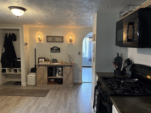 kitchen featuring dark cabinets, arched walkways, black appliances, and wood finished floors