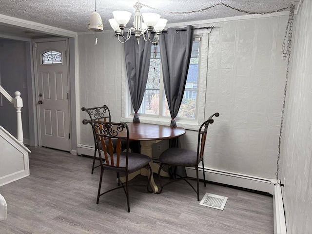 dining space featuring a baseboard radiator, a textured ceiling, a chandelier, and wood finished floors