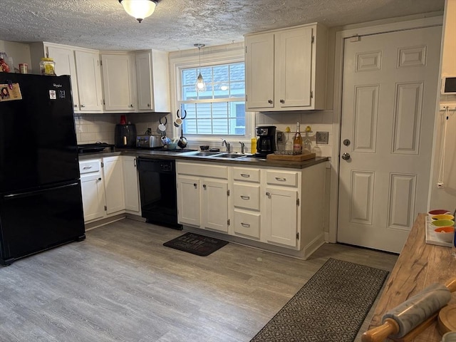 kitchen with dark countertops, light wood-type flooring, black appliances, white cabinetry, and a sink