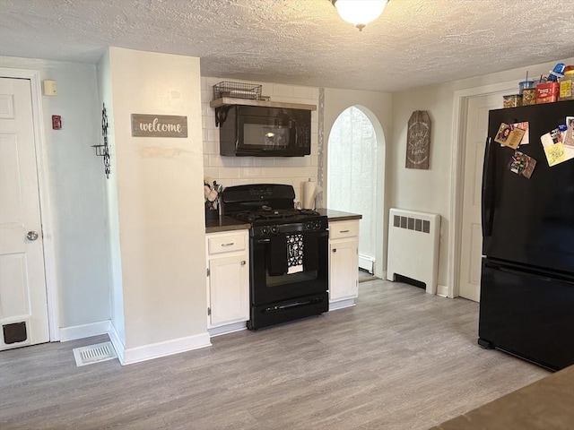 kitchen with light wood-style floors, dark countertops, radiator heating unit, black appliances, and white cabinetry