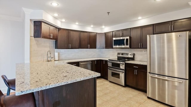 kitchen with backsplash, stainless steel appliances, light stone counters, a kitchen breakfast bar, and kitchen peninsula