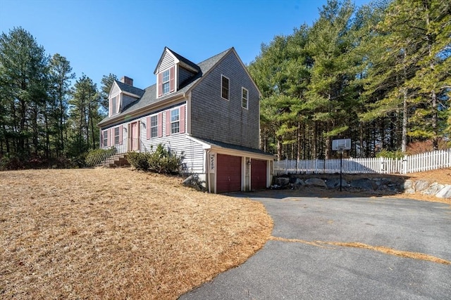 view of property exterior featuring a garage, a chimney, driveway, and fence